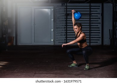 Young beautiful attractive muscular and strong fit girl holding heavy kettlebell with one hand above her head for swing or snatch hardcore crossfit workout training in the gym real people - Powered by Shutterstock