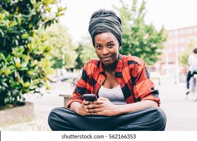 Young beautiful black woman outdoor using smart phone hand hold, looking in camera smiling - relaxing, happiness, technology concept
