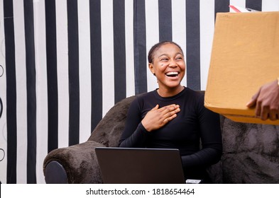 Young Beautiful Black Woman Using Her Laptop While Receiving The Delivery Of A Package To Her With Joy In Her Heart