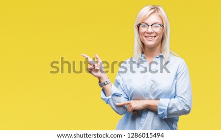 Young beautiful blonde business woman wearing glasses over isolated background with a big smile on face, pointing with hand and finger to the side looking at the camera.