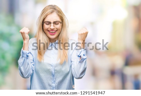 Young beautiful blonde business woman wearing glasses over isolated background excited for success with arms raised celebrating victory smiling. Winner concept.