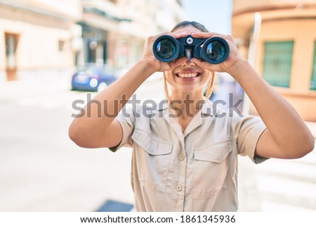Young beautiful blonde caucasian woman smiling happy outdoors on a sunny day looking through binoculars