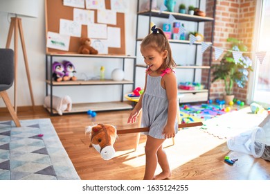 Young beautiful blonde girl kid enjoying play school with toys at kindergarten, smiling happy riding stuffed horse at home