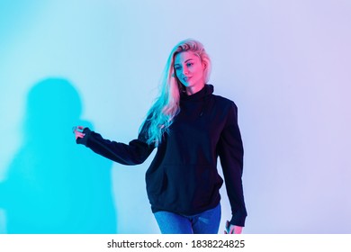 Young Beautiful Blonde Girl Model With Blond Hair In A Fashionable Black Hoodie On A Multi Color Pink-neon Background