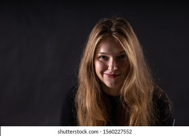 Young Beautiful Blonde Girl With A Slight Smirk On Her Face On A Dark Background