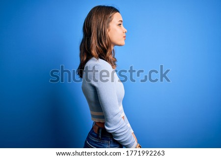 Young beautiful blonde girl wearing casual sweater standing over blue isolated background looking to side, relax profile pose with natural face with confident smile.