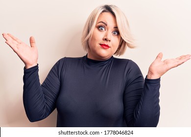 Young Beautiful Blonde Plus Size Woman Wearing Casual Sweater Over Isolated White Background Clueless And Confused With Open Arms, No Idea And Doubtful Face.