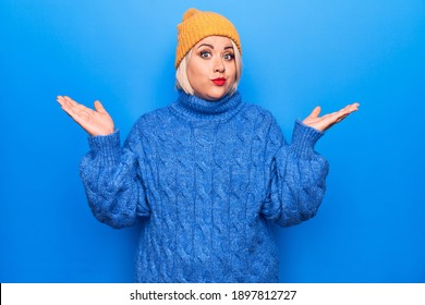 Young Beautiful Blonde Plus Size Woman Wearing Blue Casual Turtleneck Sweater And Wool Hat Clueless And Confused With Open Arms, No Idea And Doubtful Face.