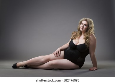 Young beautiful blonde plus size model with big natural breasts in underwear, xxl woman on gray studio background, full length portrait