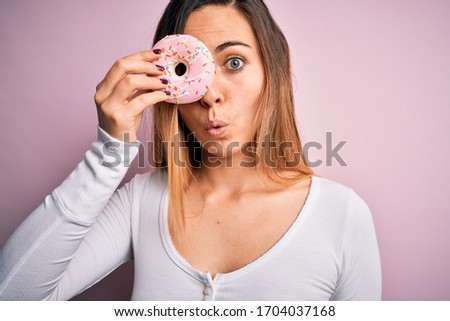 Young beautiful blonde woman with blue eyes holding pink doughnut over isolated background scared in shock with a surprise face, afraid and excited with fear expression