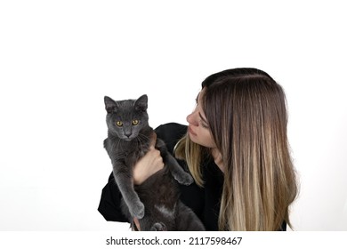 A young beautiful blonde woman closed holds young blue russian cat in her hands on a white background. Girl looking to cat. Cat looking to camera. Good friendship and pet owner. Cuddles.	