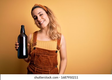 Young beautiful blonde woman drinking bottle of beer over isolated yellow background with a happy face standing and smiling with a confident smile showing teeth