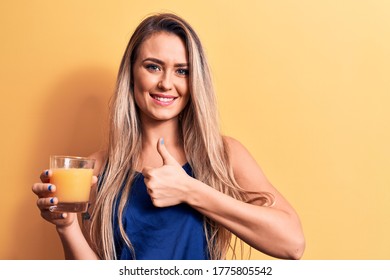 Young beautiful blonde woman drinking glass of healthy orange juice over yellow background smiling happy and positive, thumb up doing excellent and approval sign - Shutterstock ID 1775805542