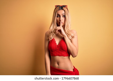 Young beautiful blonde woman on vacation wearing bikini over isolated yellow background asking to be quiet with finger on lips. Silence and secret concept.