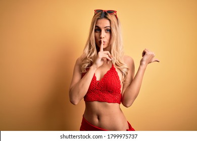 Young beautiful blonde woman on vacation wearing bikini over isolated yellow background asking to be quiet with finger on lips pointing with hand to the side. Silence and secret concept.