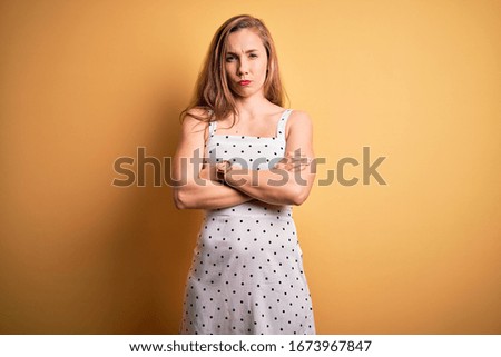 Young beautiful blonde woman on vacation wearing summer dress over yellow background skeptic and nervous, disapproving expression on face with crossed arms. Negative person.