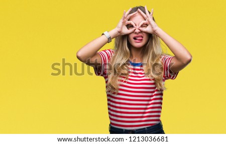 Young beautiful blonde woman over isolated background doing ok gesture like binoculars sticking tongue out, eyes looking through fingers. Crazy expression.
