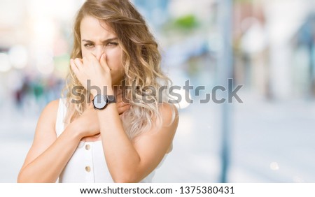 Young beautiful blonde woman over isolated background smelling something stinky and disgusting, intolerable smell, holding breath with fingers on nose. Bad smells concept.