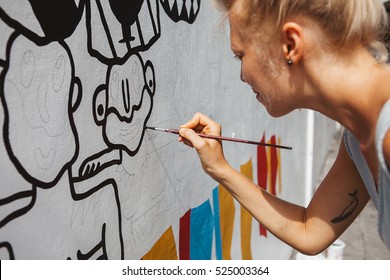 Young beautiful blonde woman painting the wall, street art in process, street artist - painter