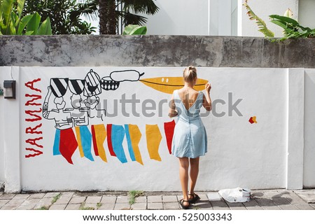 Young beautiful blonde woman painting the wall, street art in process, street artist - painter
