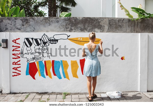 Young beautiful blonde woman\
painting the wall, street art in process, street artist -\
painter