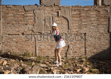 Young, beautiful, blonde, young woman playing baseball dressed in her baseball kit. Woman hits ball with baseball bat, background brick wall in a ruined building. Concept sports and olympic games