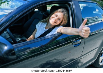 Young beautiful blonde woman smiling happy with thumb up doing ok sign sitting at the car - Shutterstock ID 1802446669