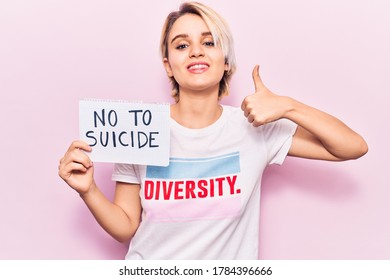 Young Beautiful Blonde Woman Wearing T Shirt With Diversity Message Holding No To Suicide Paper Smiling Happy And Positive, Thumb Up Doing Excellent And Approval Sign 