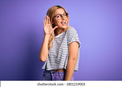 Young beautiful blonde woman wearing striped t-shirt and glasses over purple background Waiving saying hello happy and smiling, friendly welcome gesture