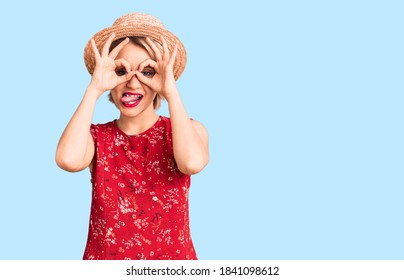 Joven y hermosa mujer rubia con sombrero de verano haciendo gesto bien como binoculares sacando la lengua, ojos mirando a través de los dedos. expresión loca. 