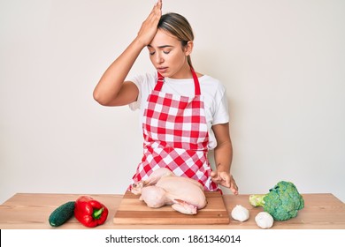 Young Beautiful Blonde Woman Wearing Apron Cooking Chicken Surprised With Hand On Head For Mistake, Remember Error. Forgot, Bad Memory Concept. 