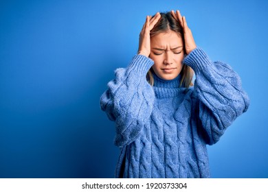 Young beautiful blonde woman wearing winter wool sweater over blue isolated background suffering from headache desperate and stressed because pain and migraine. Hands on head.