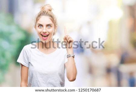 Young beautiful blonde woman wearing white t-shirt over isolated background pointing finger up with successful idea. Exited and happy. Number one.