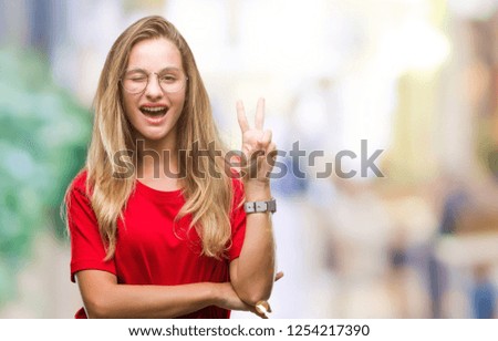 Young beautiful blonde woman wearing glasses over isolated background smiling with happy face winking at the camera doing victory sign. Number two.