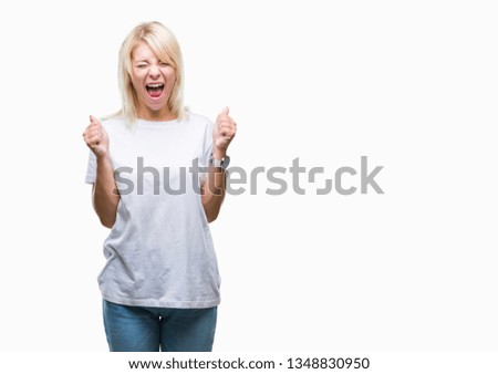 Young beautiful blonde woman wearing white t-shirt over isolated background excited for success with arms raised celebrating victory smiling. Winner concept.