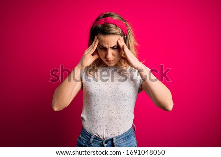 Young beautiful blonde woman wearing casual t-shirt standing over isolated pink background with hand on head for pain in head because stress. Suffering migraine.