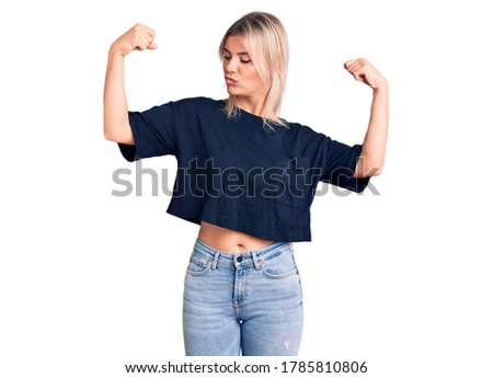 Young beautiful blonde woman wearing casual t-shirt showing arms muscles smiling proud. fitness concept. 