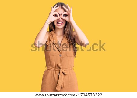 Young beautiful blonde woman wearing casual clothes and glasses doing ok gesture like binoculars sticking tongue out, eyes looking through fingers. crazy expression. 