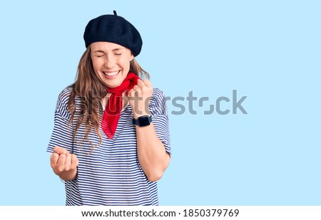 Young beautiful blonde woman wearing french beret and striped t-shirt celebrating surprised and amazed for success with arms raised and eyes closed. winner concept. 