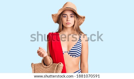 Young beautiful blonde woman wearing bikini and hat holding summer wicker handbag thinking attitude and sober expression looking self confident 