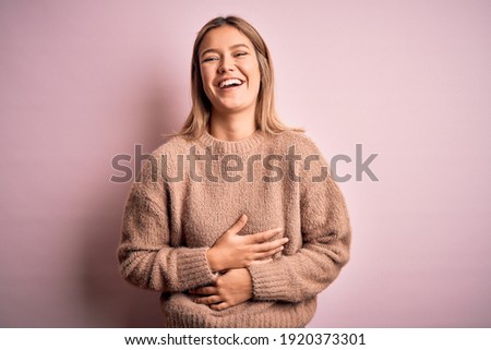 Young beautiful blonde woman wearing winter wool sweater over pink isolated background smiling and laughing hard out loud because funny crazy joke with hands on body.