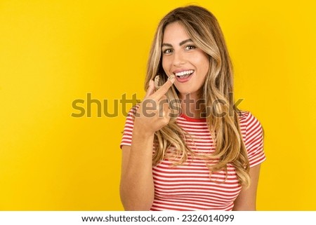 Young beautiful blonde woman wearing striped t-shirt over yellow studio background holding an invisible aligner ready to use it. Dental healthcare and confidence concept.