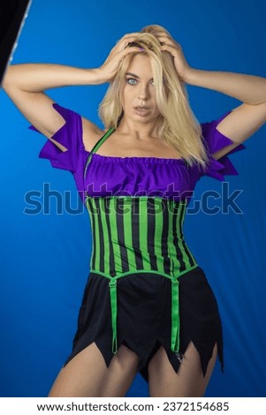 Young beautiful blonde woman in a witch costume on a blue background. Short dress, long hair. Halloween concept. Soft focus