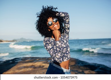 Young beautiful Brazilian girl staying on beach in Rio de Janeiro on warm sunny with embankment and tall residential houses in blurred background and laughing