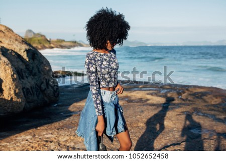 Young beautiful Brazilian girl staying on beach in Rio de Janeiro on warm sunny with embankment and tall residential houses in blurred background