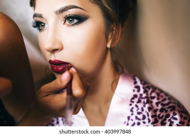 Young Beautiful Bride In A Satin Dressing Gown Doing Makeup With Burgundy Lipstick