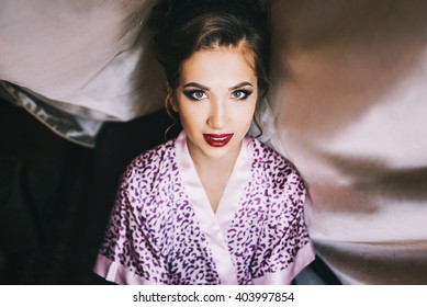 Young Beautiful Bride In A Satin Dressing Gown Doing Makeup With Burgundy Lipstick