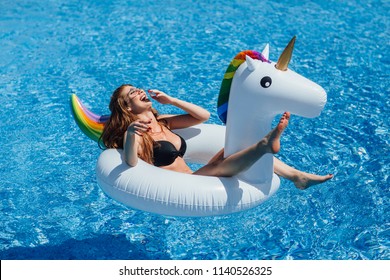 Young beautiful brown-haired girl with a good figure tan in the pool on an inflatable unicorn in a black swimsuit.