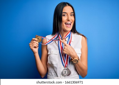 Young Beautiful Brunette Atthete Champion Woman Winning Medals Over Blue Background Very Happy Pointing With Hand And Finger