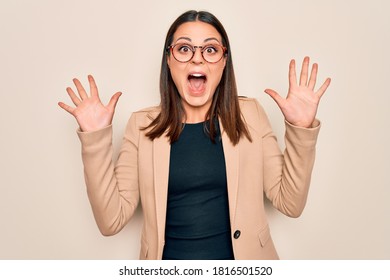 Young beautiful brunette businesswoman wearing jacket and glasses over white background celebrating crazy and amazed for success with arms raised and open eyes screaming excited. Winner concept - Shutterstock ID 1816501520